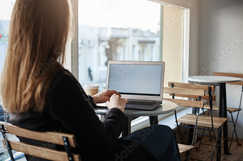 Time to be productive. Rearview of successful female freelancer in stylish clothes sitting in cafe while working in laptop and waiting for order, creating design of main site of company she works for