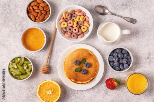 Breakfast with colorful cereal rings, pancakes, fruit, milk, juice.