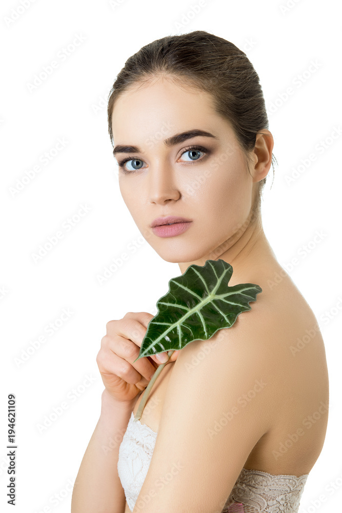 Gorgeous girl with cleann skin and perfect hair holding green fresh leaf on her shoulder, studio shot isolated on white background. Beautiful young woman's portrait. Care of mother-nature. Gorgeous girl with cleann skin and perfect hair holding green fresh leaf on her shoulder, studio shot isolated on white background. Beautiful young woman's portrait. Care of mother-nature.