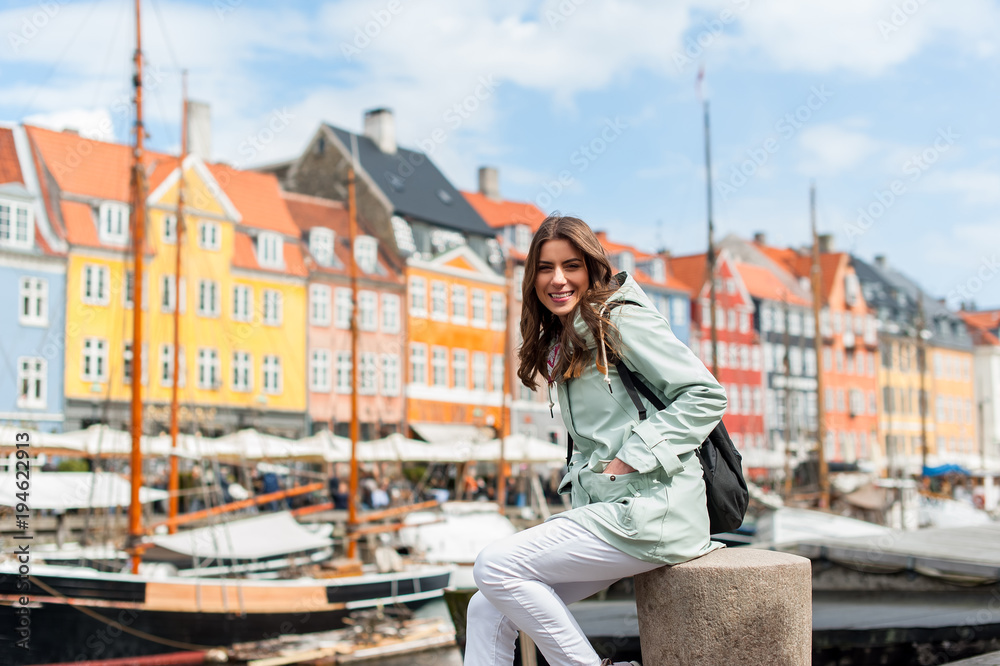 Happy young tourist woman with backpack at Copenhagen, Nyhavn, Denmark. Visiting Scandinavia, famous European destination during fall or spring. Travel and Lifestyle.