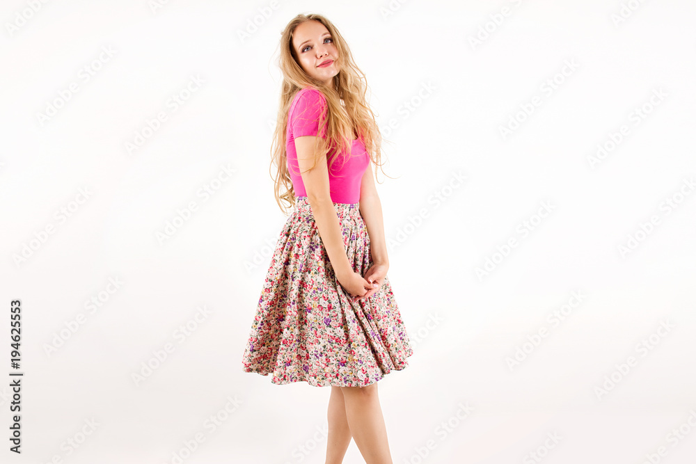young cutest blonde girl in a pink combination and skirt with flowers with long hair curls standing and smiling like a barbie hesitates on a white wall background young cutest blonde girl in a pink combination and skirt with flowers with long hair curls standing and smiling like a barbie hesitates on a white wall background
