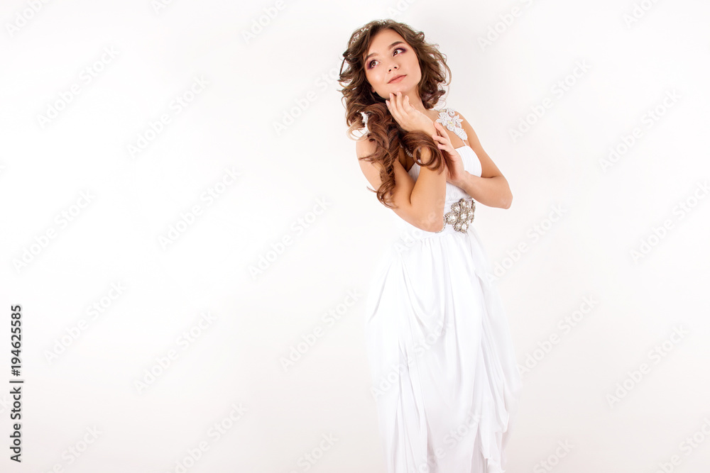 young girl in a white airy wedding dress with big curls standing like angel and smiling on a white wall background young girl in a white airy wedding dress with big curls standing like angel and smiling on a white wall background