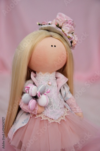 beautiful doll toy with a biscuit in hands on a pink background close-up