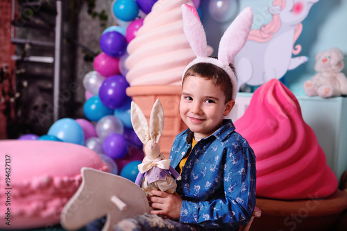 baby boy with rabbit ears with easter bunny in hands smiling sitting on wooden horse