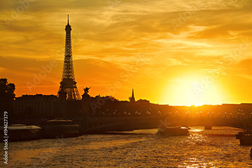 Sunset view of Paris with the Eiffel Tower and the Pont Alexandre III bridge over the river Seine with picturesque sky and a boat moving under the bridge, France © Dmitrii