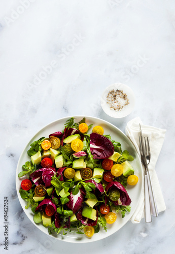 summer bright fresh salad of cherry tomatoes, avocado and radicchio leaves on a white marble table. concept of healthy eating. copy space
