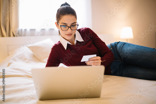 Young girl laying down on the bed and shopping online.