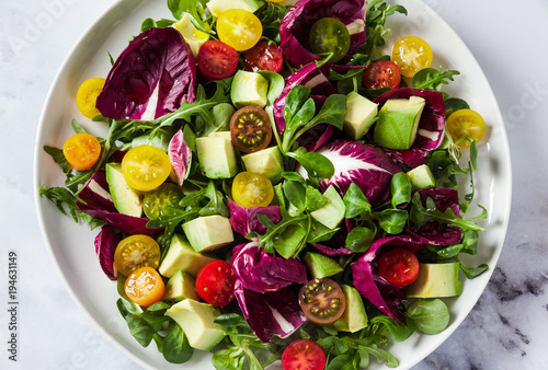 summer bright fresh salad of cherry tomatoes, avocado and radicchio leaves on a white marble table. concept of healthy eating. photo