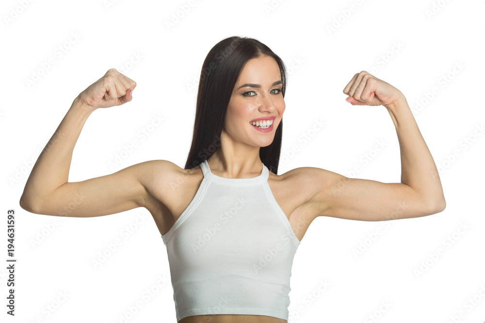 beautiful young joyful girl with a smile in a white tank top on a white background showing her muscles in her arms beautiful young joyful girl with a smile in a white tank top on a white background showing her muscles in her arms
