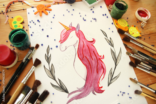 drawing of a unicorn watercolor with paints and brushes on a wooden background