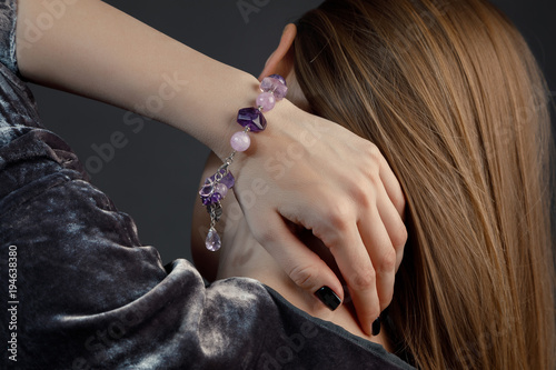 женская кисть руки с черным лаком на ногтях и красивым браслетом из сиреневых драгоценных камней на шее в волосах у женщины 