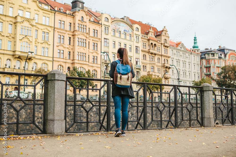 A beautiful tourist girl with a backpack admiring the ancient architecture of Prague in the Czech Republic.