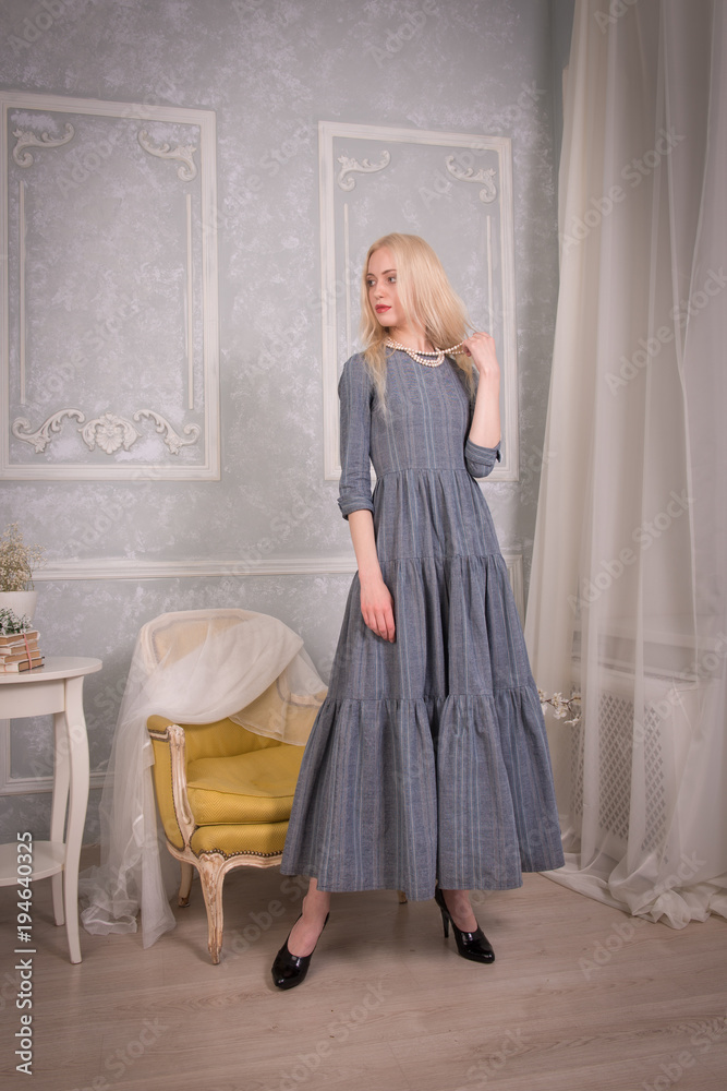 Blonde girl in long grey retro dress stands gracefully in vintage interiors Blonde girl in long grey retro dress stands gracefully in vintage interiors