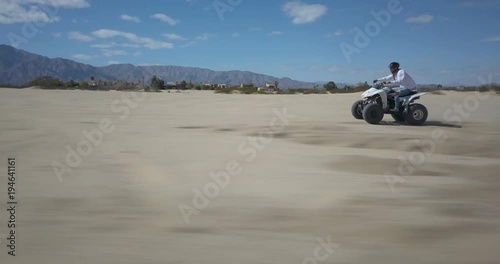 Wallpaper Mural Fast aerial dolly shot to the left of an ATV bouncing over tracks in the sand with mountains in the distance under a clear blue sky. Torontodigital.ca