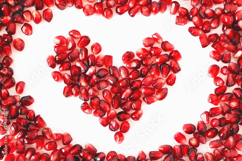 Heart shaped pomegranate seeds on white background. Love, Valentines day and healthy life concept, flat lay top view. Pomegranate seeds in a shape of a heart.Red heart isolated on the white background