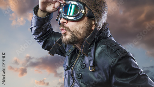 Explore pilot of the 20s with sunglasses and vintage aviator helmet. Wears leather jacket, beard and expressive faces © Fernando Cortés