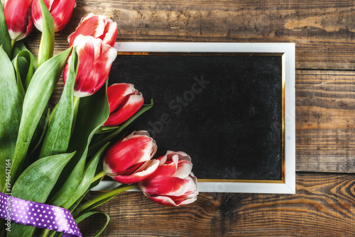 Background for congratulations, greeting cards. Fresh spring tulips flowers with chalkboard for text, on a wooden background top view copy space