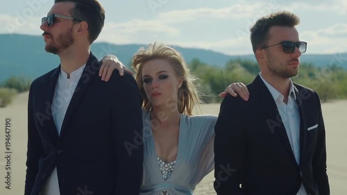 Blonde is standing between two boyfriends in a desert. Strange relationships of woman with two man, abstract shot on a beach