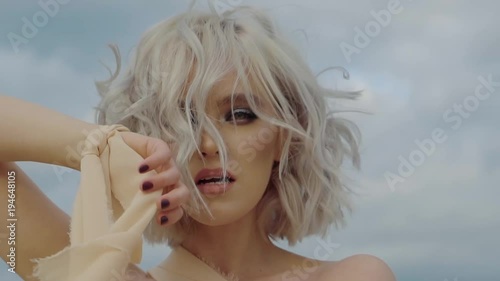 Fashion model is expressing emotions on her face and looking in camera. Close-up of her face with bright makeup and hairstyle, waving fabric of clothes