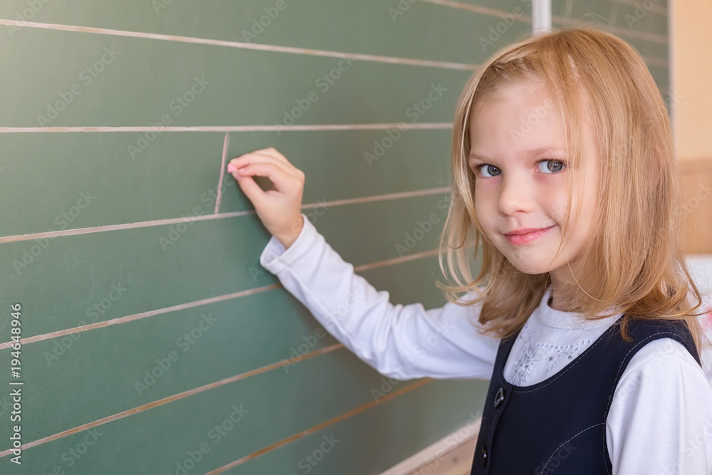 First grade pupil a girl writing on green blackboard at school lesson First grade pupil a girl writing on green blackboard at school lesson