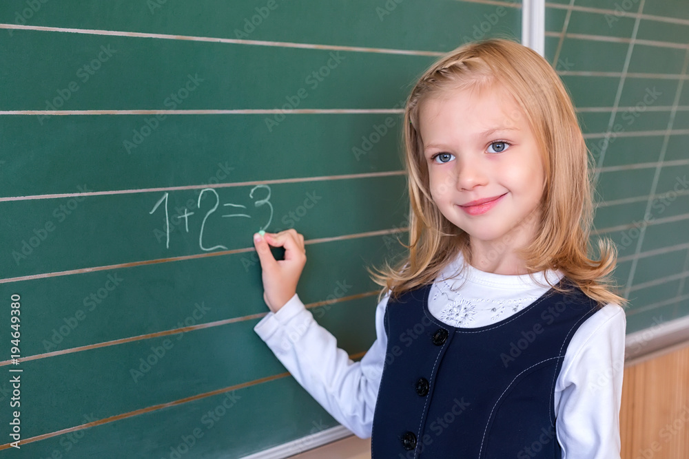 First grade pupil a girl writing on green blackboard at school lesson First grade pupil a girl writing on green blackboard at school lesson