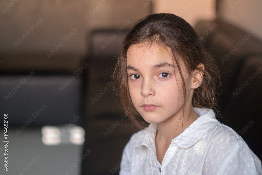 little beautiful girl dressed in school shirt sitting on sofa in front of window little beautiful girl dressed in school shirt sitting on sofa in front of window