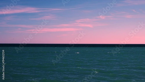 We see across the lake to its horizon. The lake is teal with the black almost edge and a bright blue ridge sky with Crimson clouds. At the end we tilter to the sky. photo