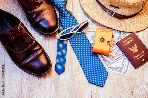 Top view accessories for travel on old wood, Shells, yellow camera ,shoes ,glasses necktie , hat ,and Dollar on Thailand passport. photo concept travel and life style. 