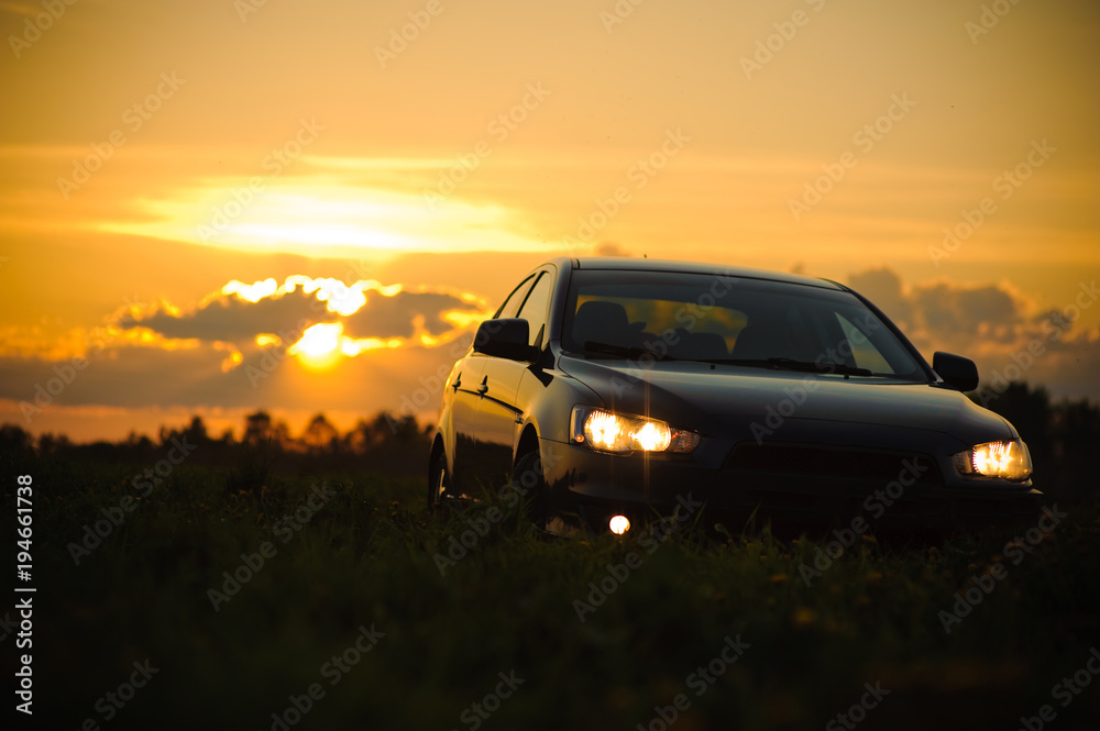 Blue sport car with headlights in a field in bright sunset light at summer evening
