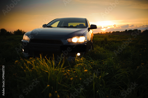 Blue sport car with headlights in a field in bright sunset light at summer evening © ANR Production