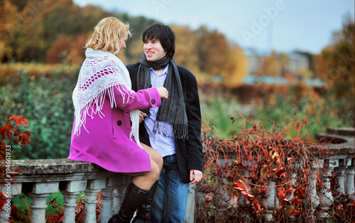 Love story of young beautiful couple in Peterhof, Saint-Petersburg, Russia at autumn. Blonde girl in pink coat and blue dress and man or groom in black jacket and jeans. Embrace kiss with fall in love photo