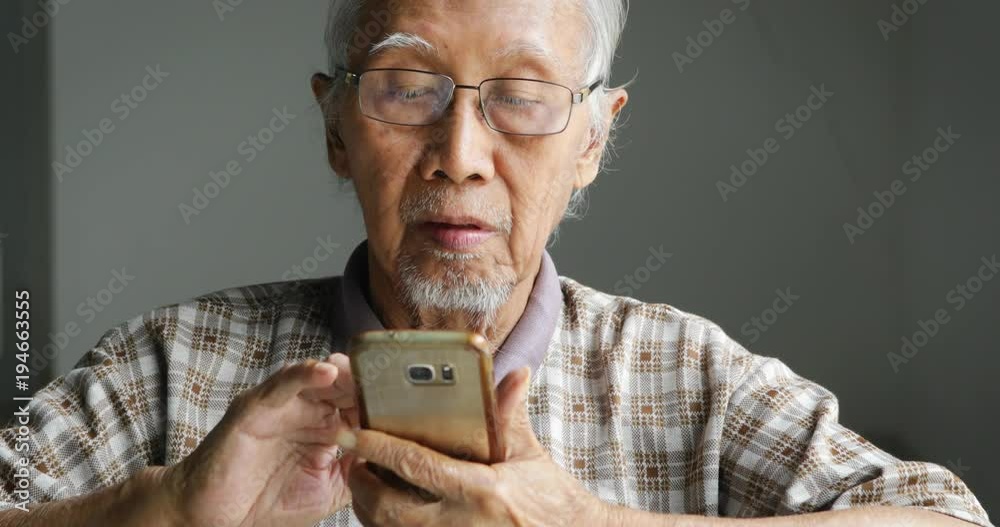 Senior man with grizzled hair, wearing glasses and using a smartphone at home. Shot in 4k resolution Senior man with grizzled hair, wearing glasses and using a smartphone at home. Shot in 4k resolution