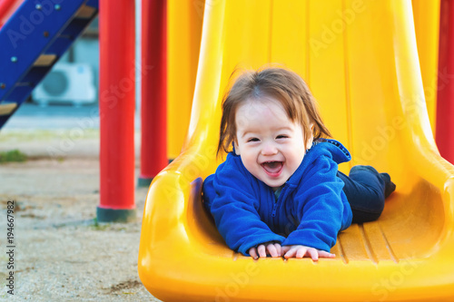 Happy toddler boy playing on a slide at a playground