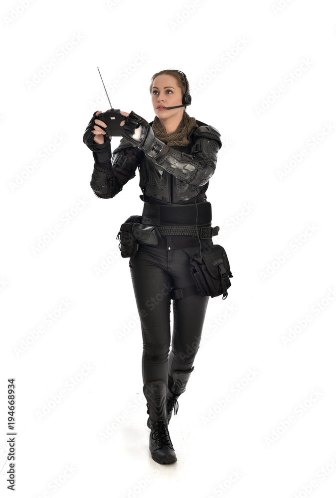 full length portrait of female soldier wearing black tactical armour, holding a remote control, isolated on white studio background. full length portrait of female soldier wearing black tactical armour, holding a remote control, isolated on white studio background.