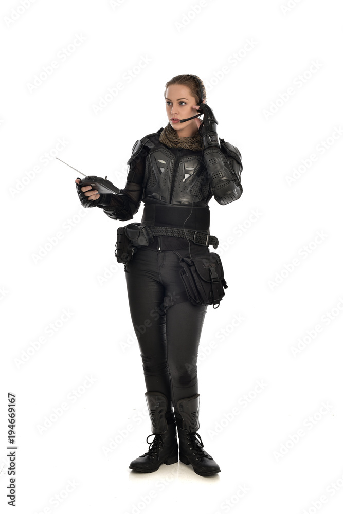 full length portrait of female soldier wearing black tactical armour, holding a remote control, isolated on white studio background. full length portrait of female soldier wearing black tactical armour, holding a remote control, isolated on white studio background.