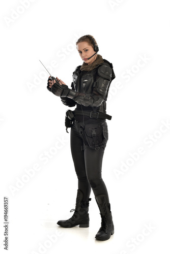 full length portrait of female soldier wearing black tactical armour, holding a remote control, isolated on white studio background.