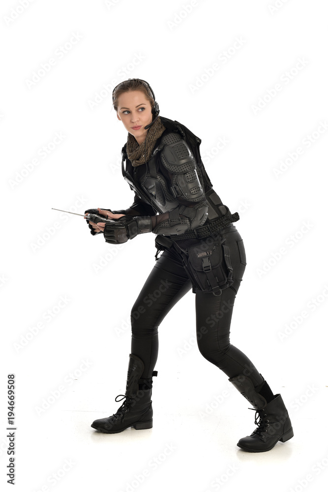 full length portrait of female soldier wearing black tactical armour, holding a remote control, isolated on white studio background. full length portrait of female soldier wearing black tactical armour, holding a remote control, isolated on white studio background.