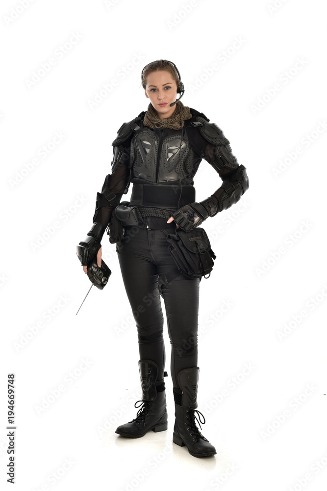 full length portrait of female soldier wearing black tactical armour, holding a remote control, isolated on white studio background. full length portrait of female soldier wearing black tactical armour, holding a remote control, isolated on white studio background.