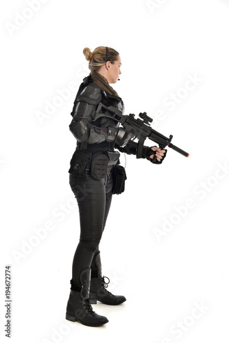 full length portrait of female soldier wearing black tactical armour, holding a rifle gun, isolated on white studio background.