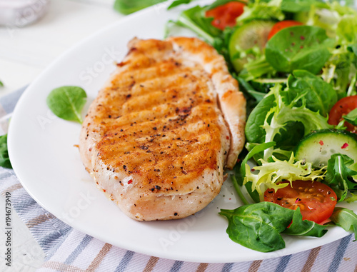 Grilled chicken breast and fresh vegetable salad - tomatoes, cucumbers and lettuce leaves. Chicken salad. Healthy food.