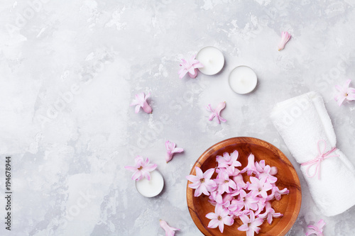 Beauty, aromatherapy and spa background with perfumed pink flowers water in wooden bowl and candles on stone table. Top view, flat lay.