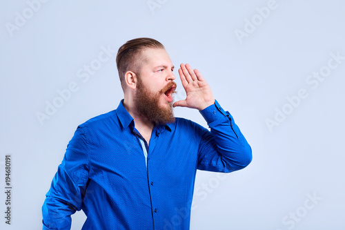 Bearded man in casual clothes on a gray background shouts. photo