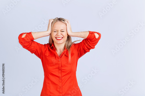 Young blond woman in an everyday with headache problems on a gray background.