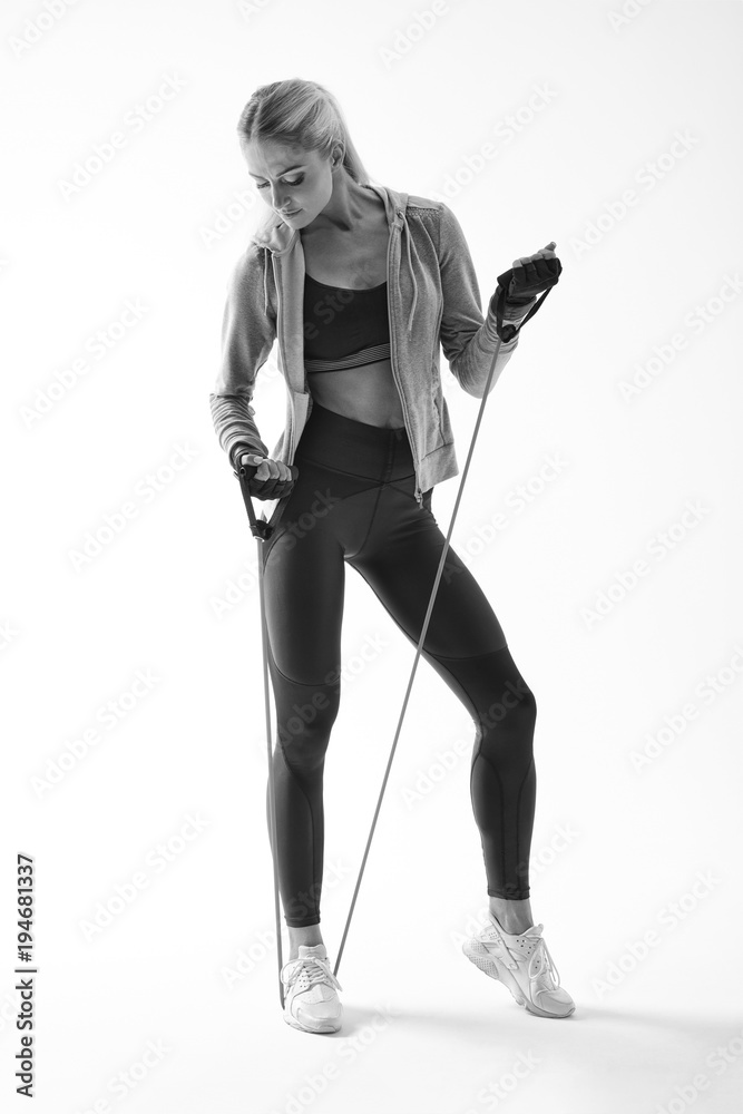 Black and white full length shot of fit young female fitness model Resistance band arms workout Attractive woman athlete in sportswear standing with resistance band on white background Black and white full length shot of fit young female fitness model Resistance band arms workout Attractive woman athlete in sportswear standing with resistance band on white background