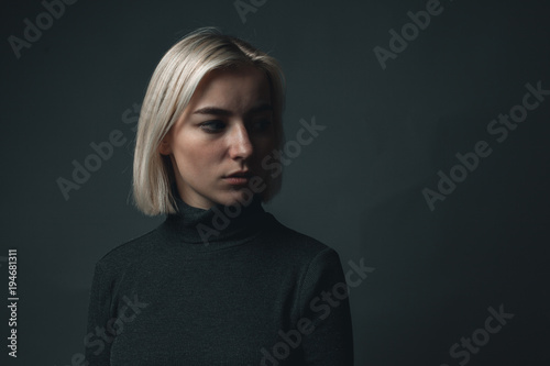 young blond female is posing near black background. low key