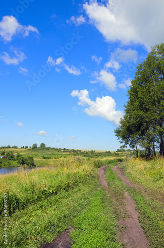 Sunny summer landscape with dirt rural road.Bright blue sky with white clouds.Countryside.Tula region Russia.