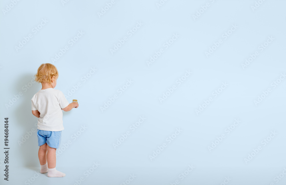 Little boy with paint brush standing back near blue wall Little boy with paint brush standing back near blue wall