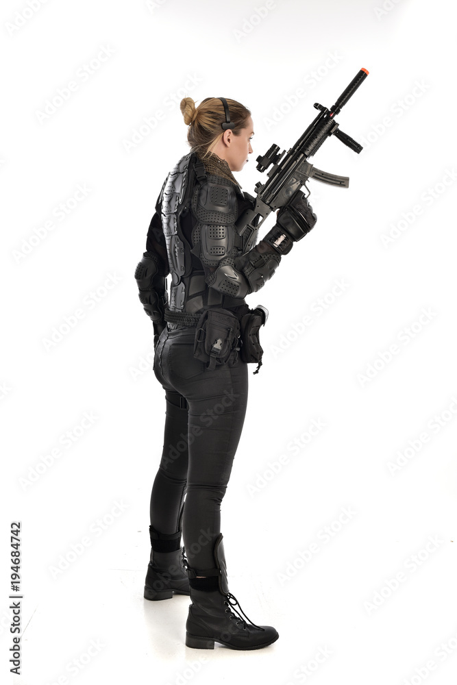 full length portrait of female soldier wearing black tactical armour, holding a rifle gun, isolated on white studio background. full length portrait of female soldier wearing black tactical armour, holding a rifle gun, isolated on white studio background.