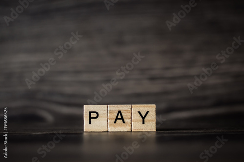 the word pay, consisting of light wooden cubes on a dark wooden background photo