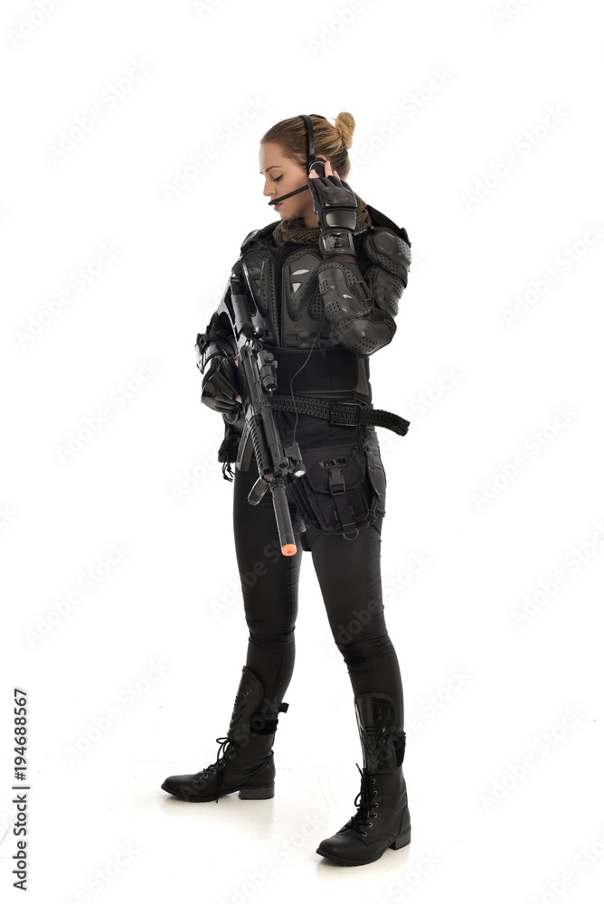 full length portrait of female  soldier wearing black  tactical armour, holding a rifle gun, isolated on white studio background.